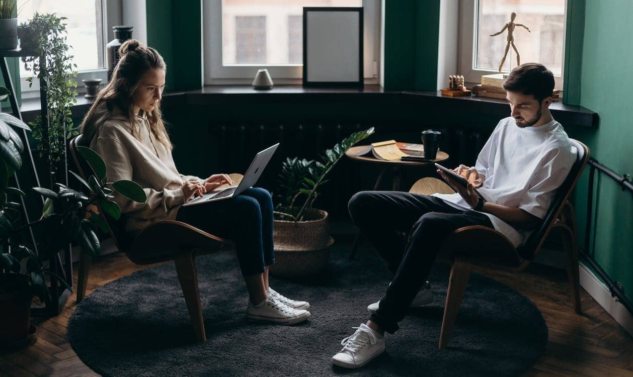 Two people working on laptops and tablets indoors.