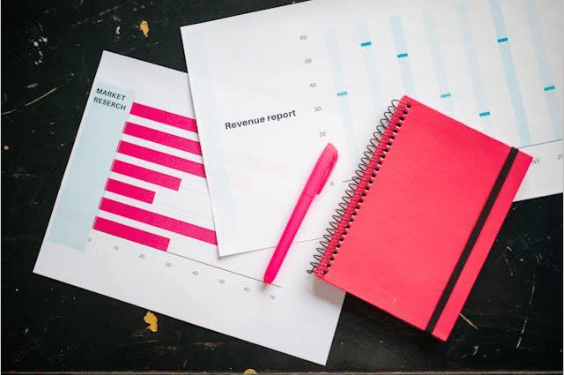 Pink notebook and pen placed on a black surface alongside papers